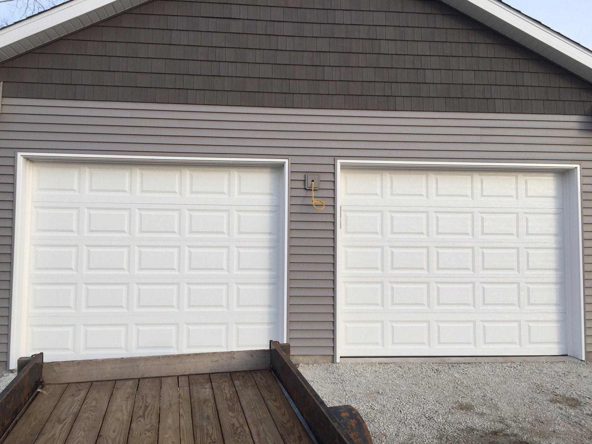 A garage with two white garage doors and a trailer parked in front of it