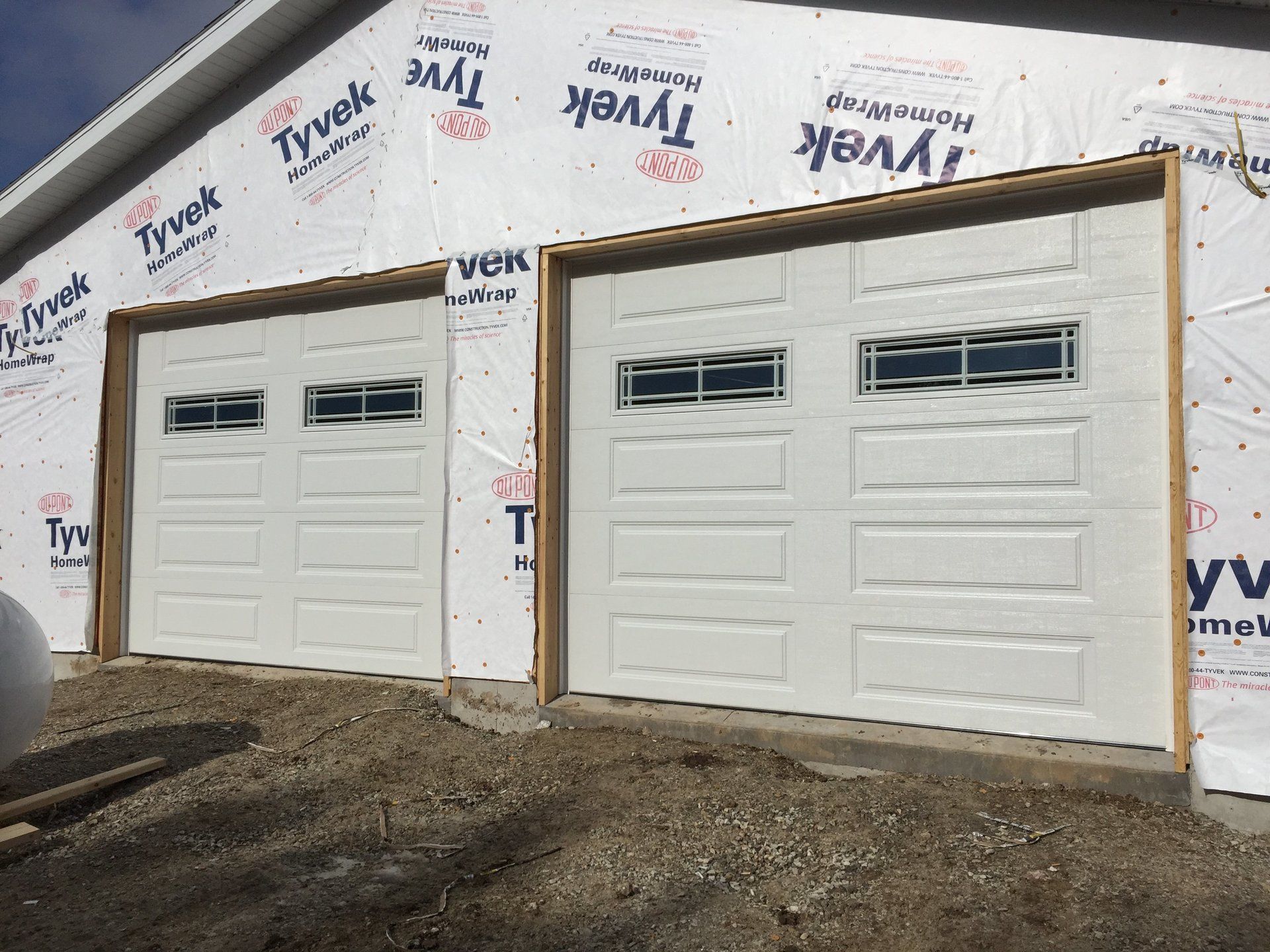 Two white garage doors are being installed on the side of a building.