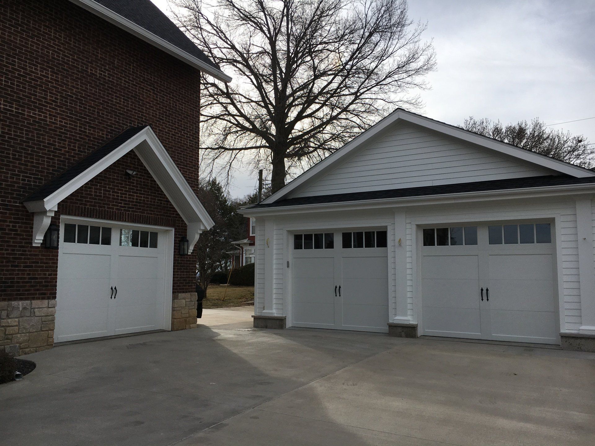 Two white garage doors are next to each other in front of a brick house.