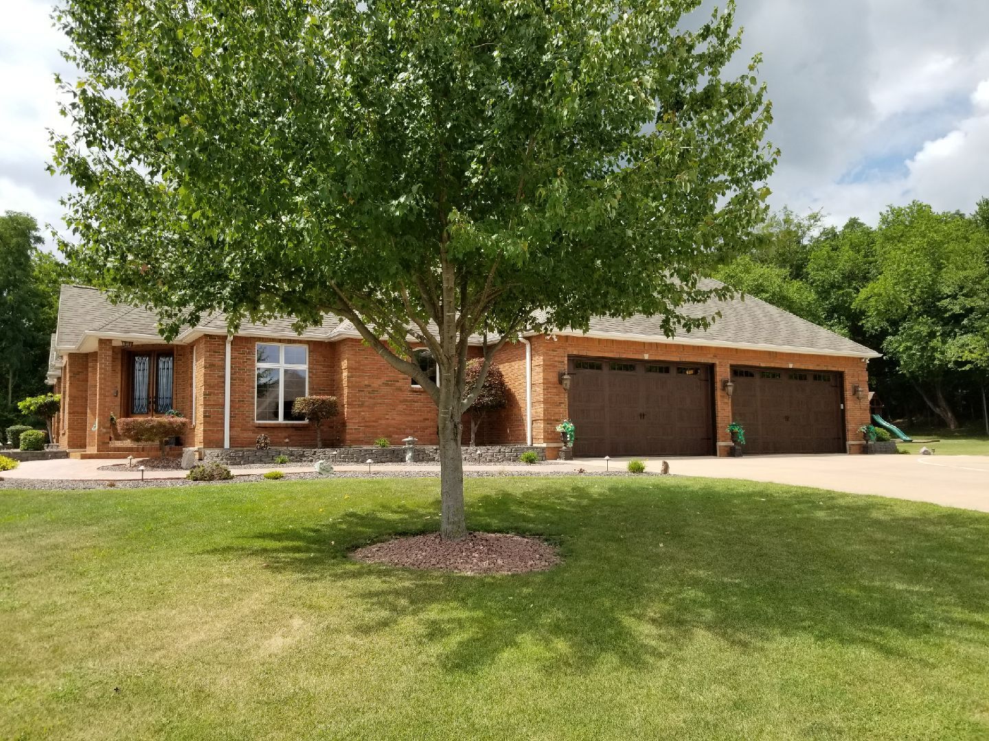 A brick house with two garages and a tree in front of it.