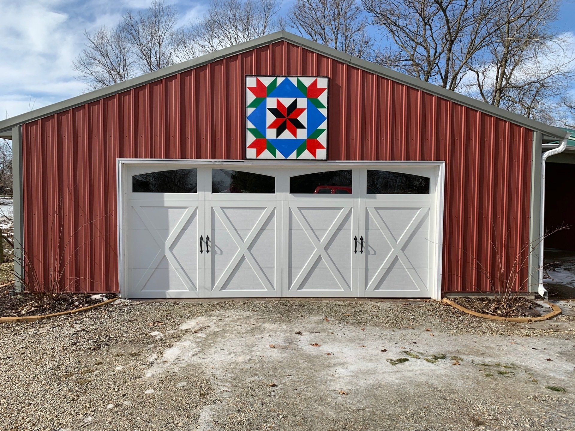 A red garage with white doors and a barn quilt on it