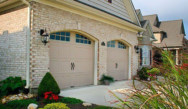There are two garage doors on the side of a brick house.