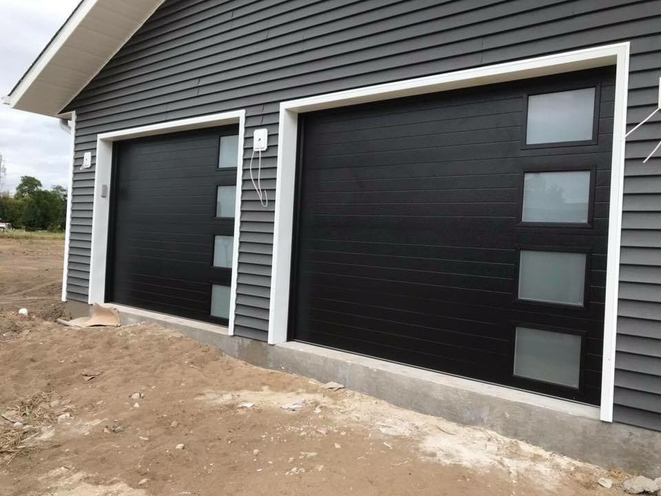 A pair of black garage doors are sitting on the side of a house.