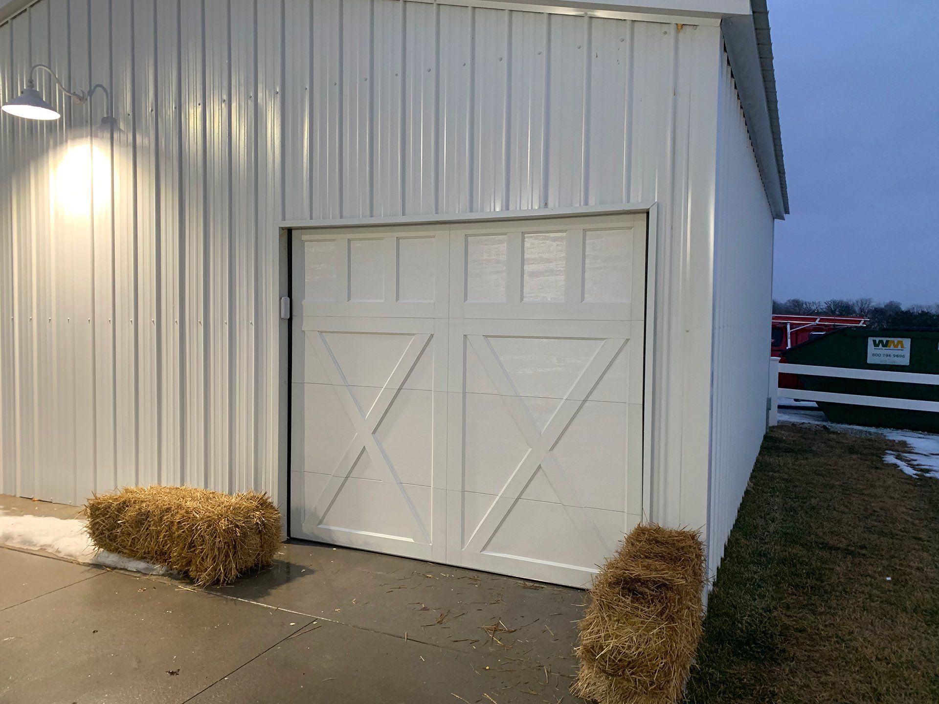 A white barn with a garage door and hay bales in front of it.
