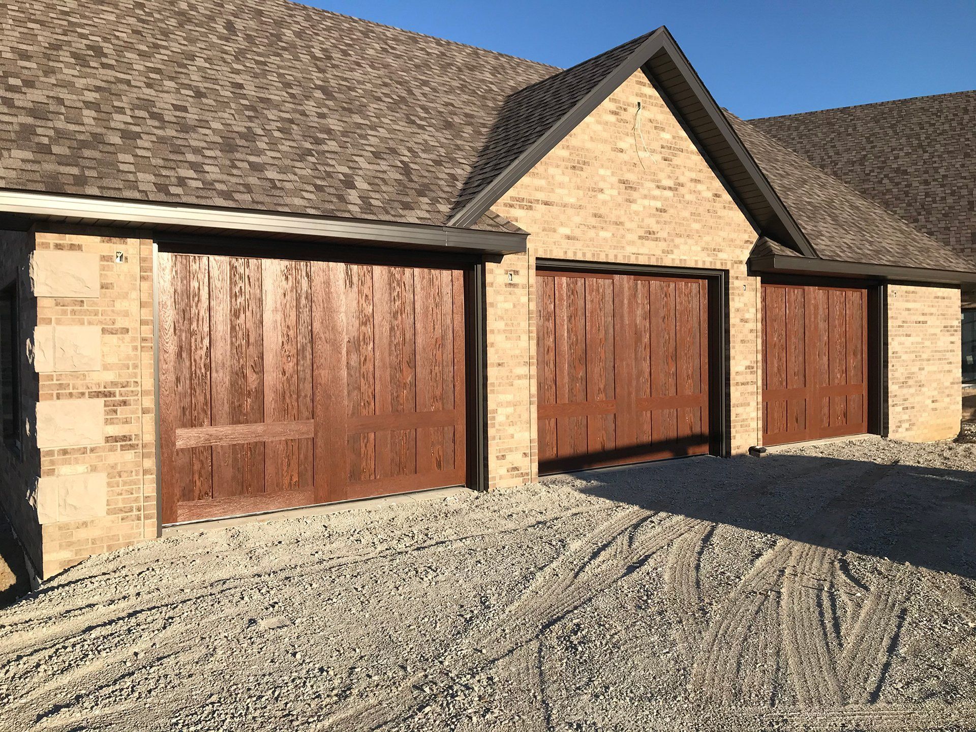 A brick house with two wooden garage doors and a gravel driveway.