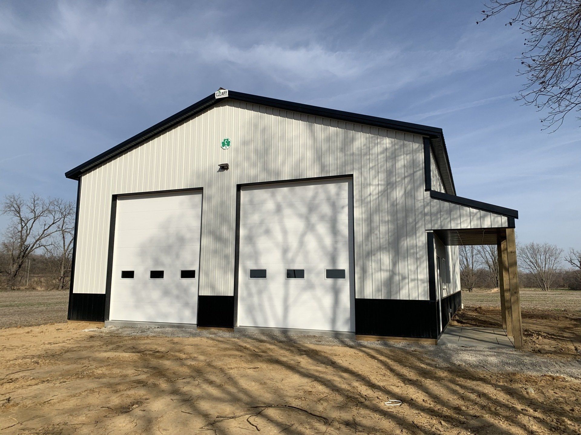 A white garage with black trim is sitting in the middle of a dirt field.
