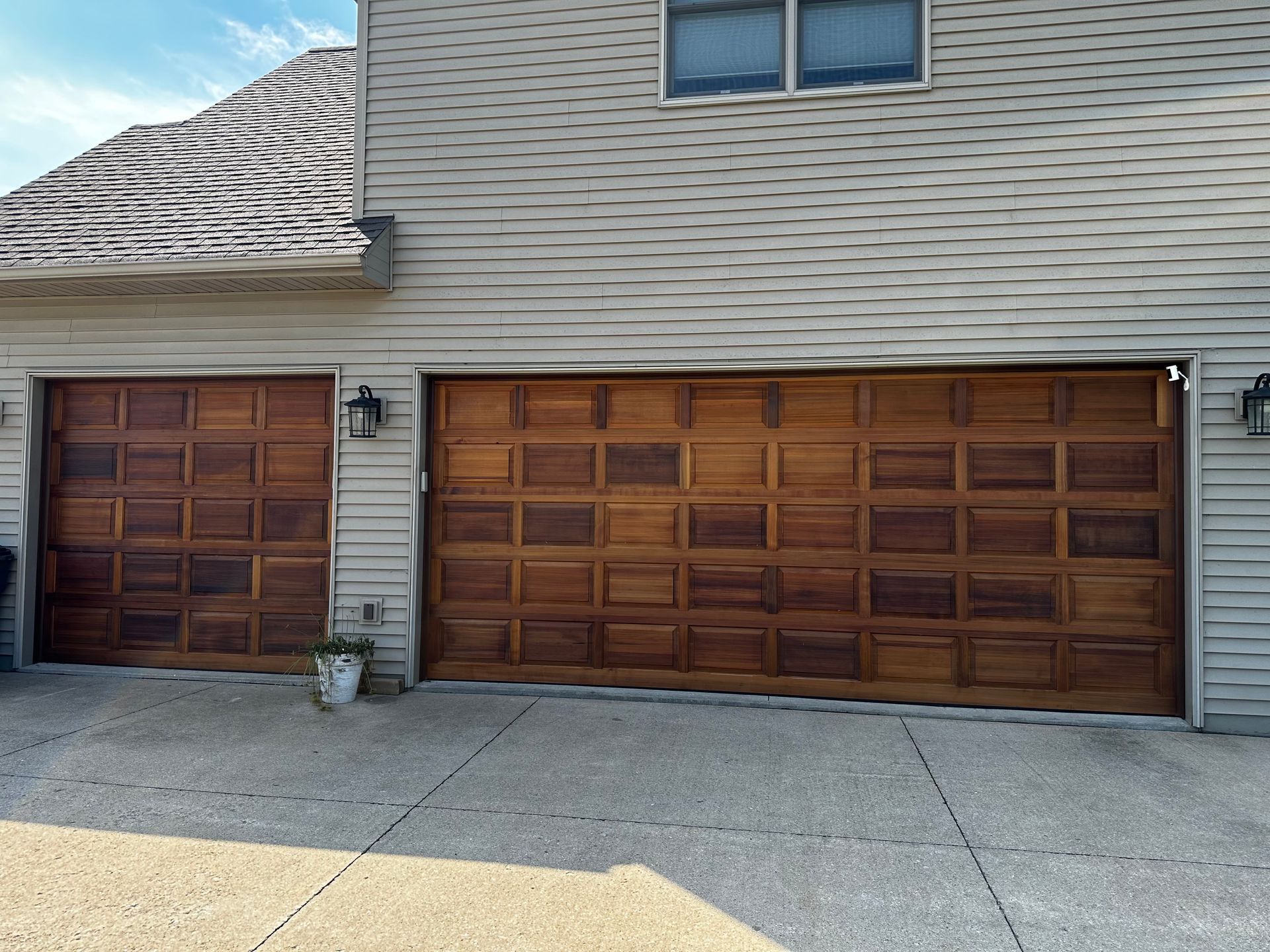 A house with two wooden garage doors and a potted plant in front of it.
