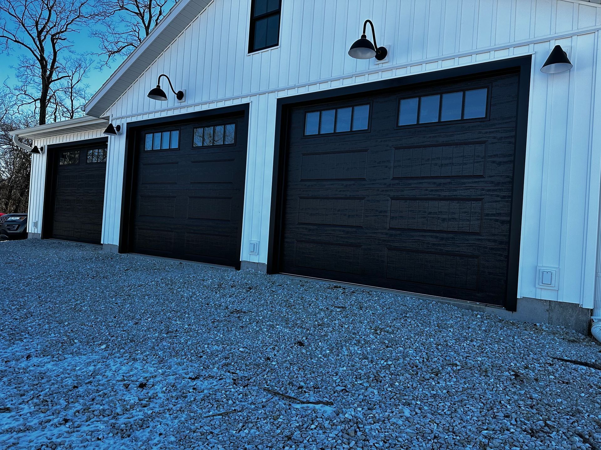 Three black garage doors are lined up in front of a white building.