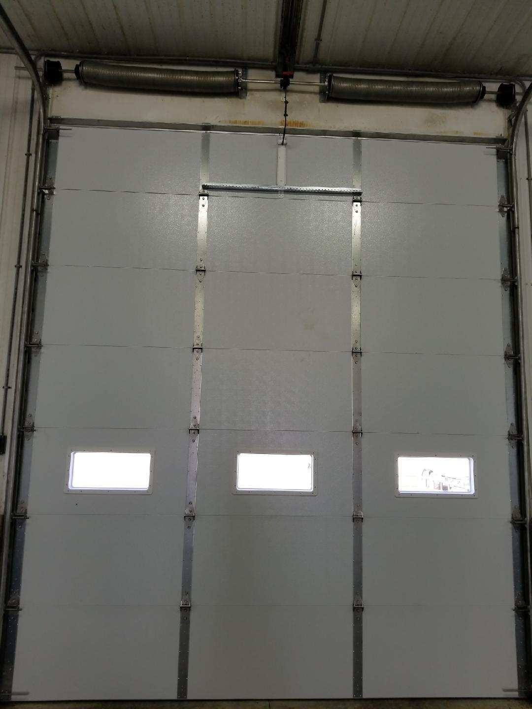 A white garage door with three windows is open in a building.