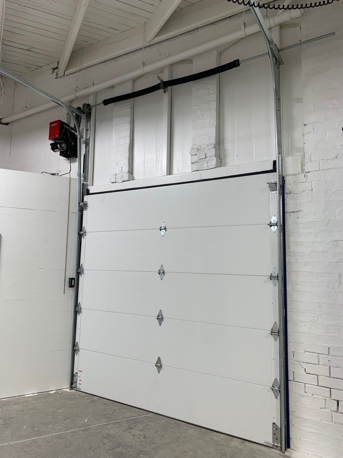A white garage door is open in a warehouse.