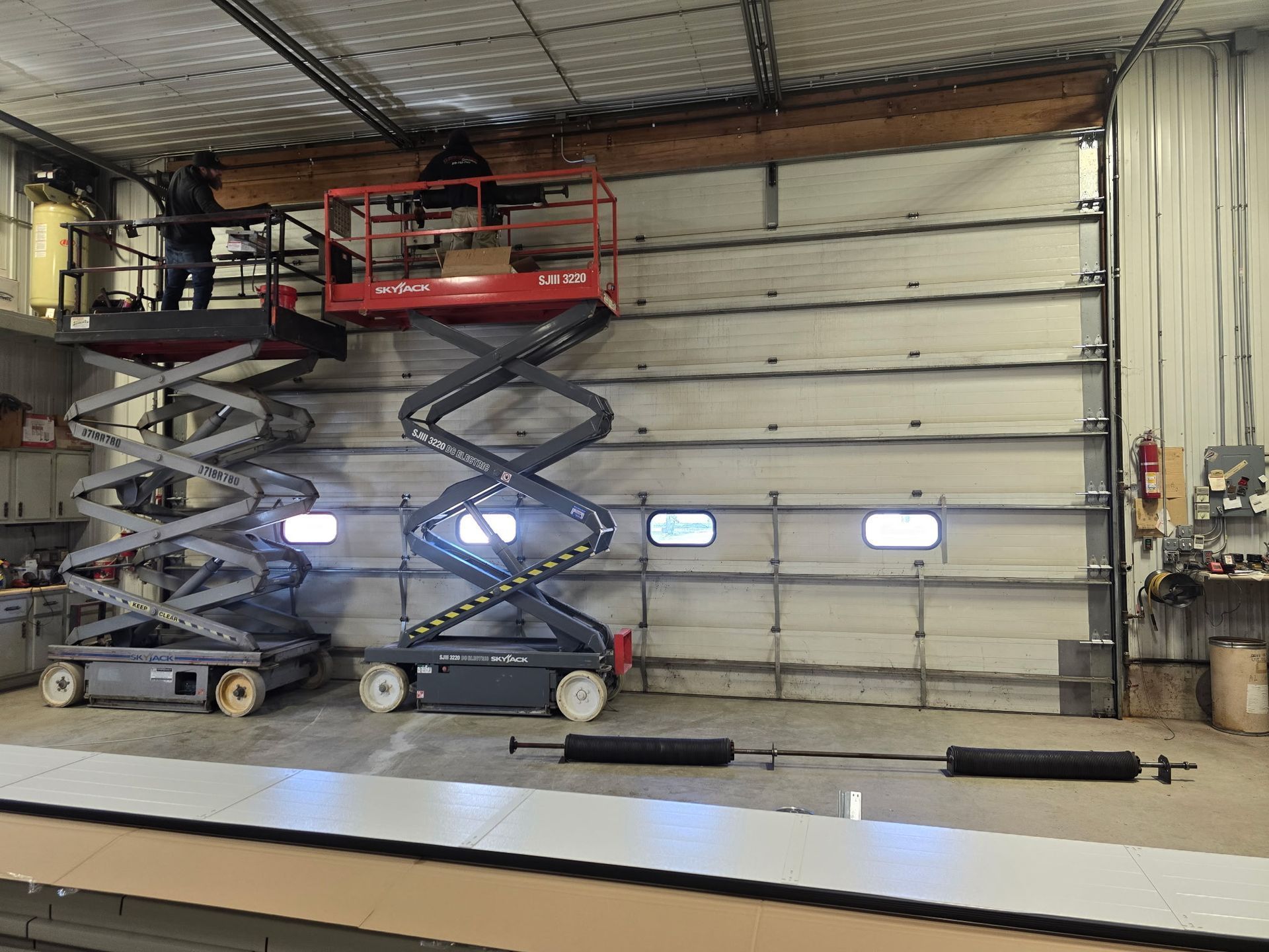 A man is standing on a scissor lift in front of a garage door.
