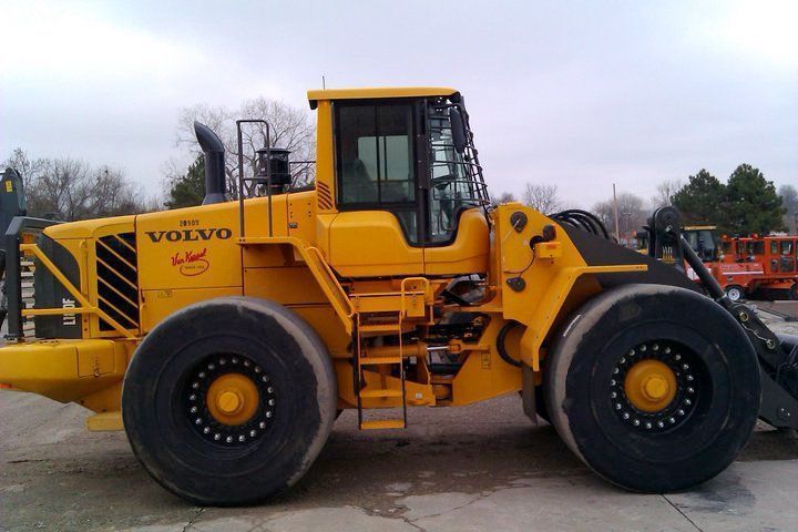 Yellow Volvo wheel loader parked on a lot, side view with large black tires and raised bucket arm