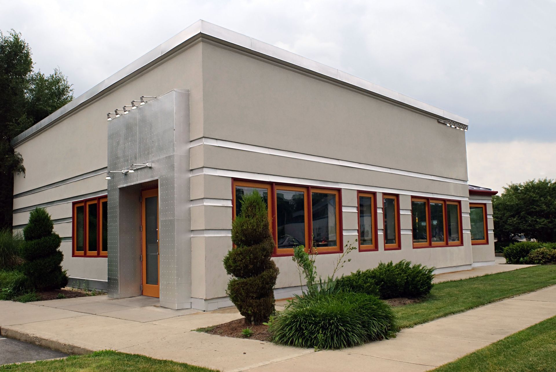 Small modern commercial building with beige walls, orange-trimmed windows, and a sidewalk entrance