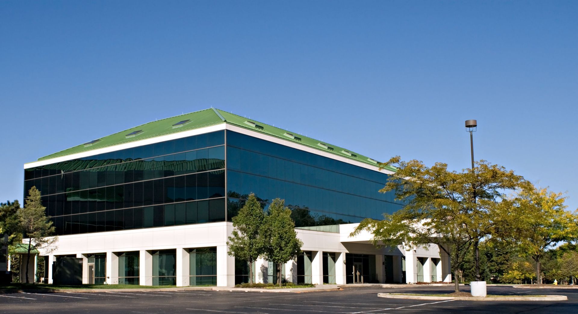 Modern glass office building with green roof and white columns beside a parking lot