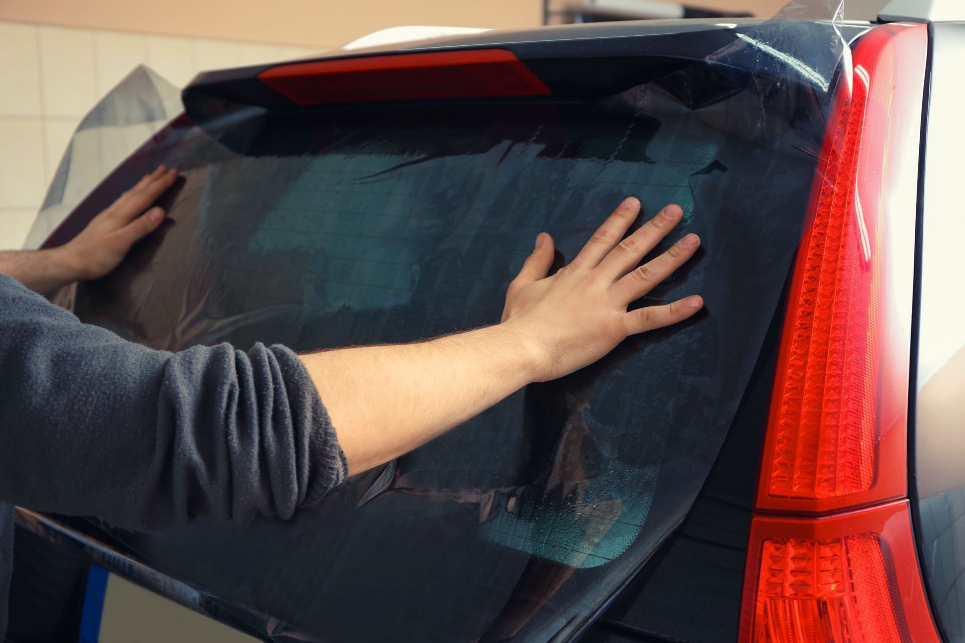 Person pressing both hands against a car’s rear window next to a red taillight.