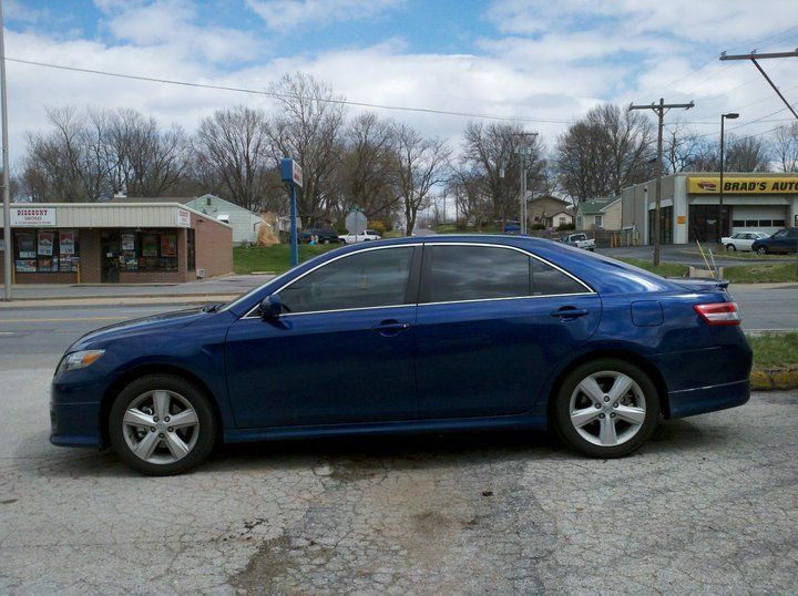 Blue sedan parked on a street in front of shops under a cloudy sky