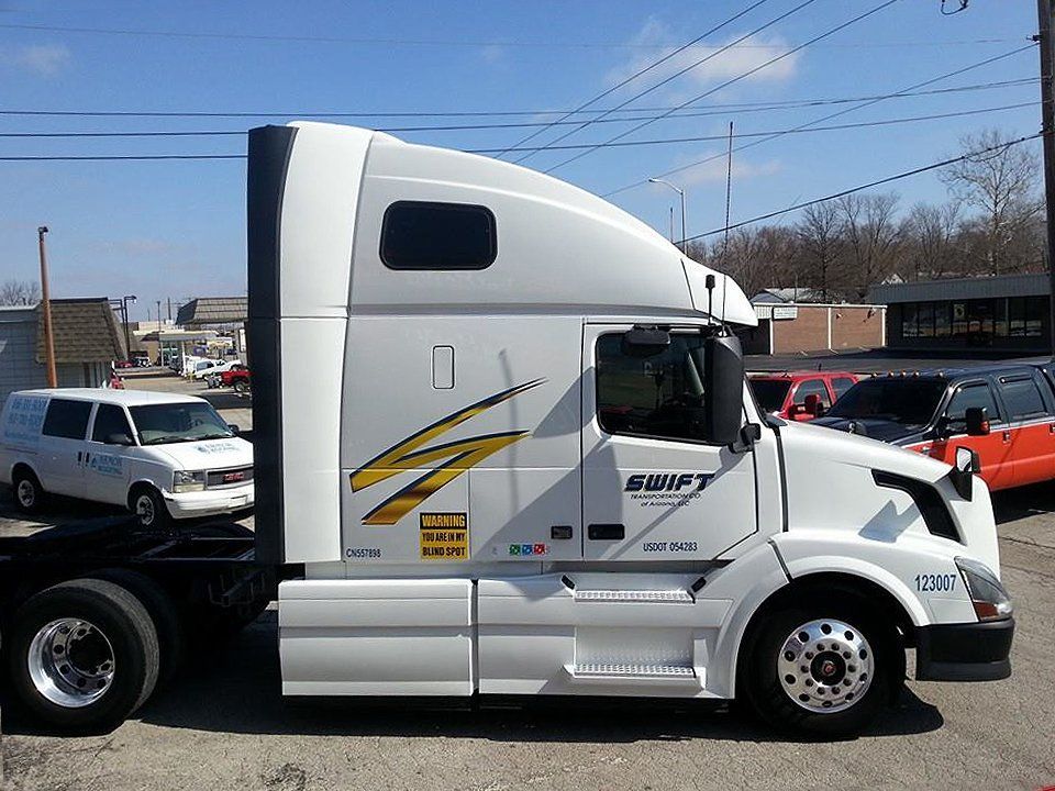 White semi-truck cab with sleeper parked outdoors on a sunny lot, side view