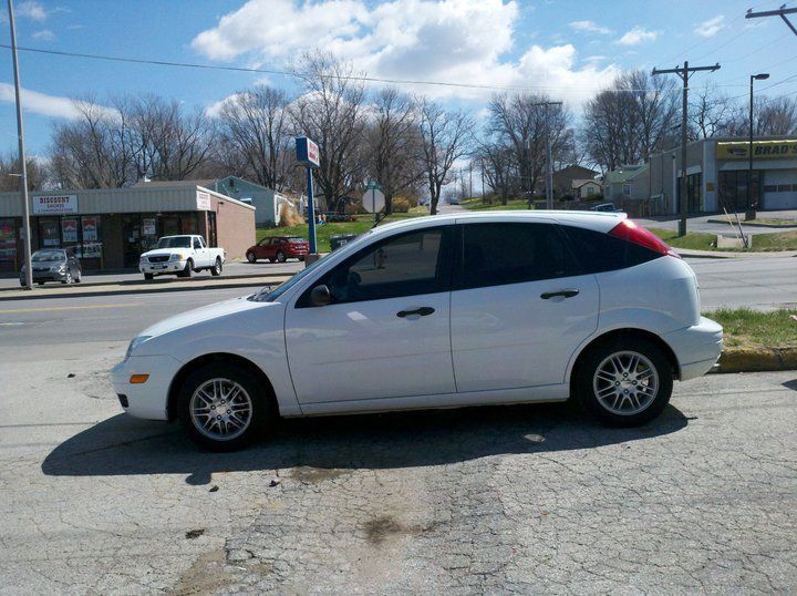 White hatchback car parked on a street in front of shops under a blue sky