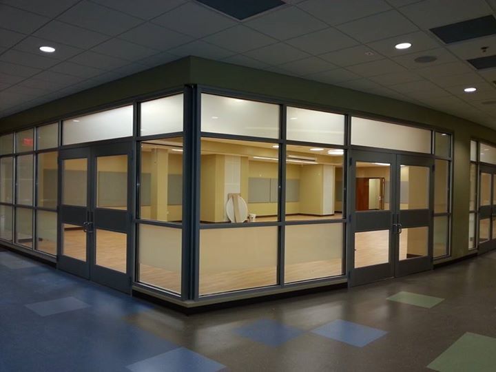 Glass-walled office suite in a dim hallway with blue-gray flooring and ceiling lights
