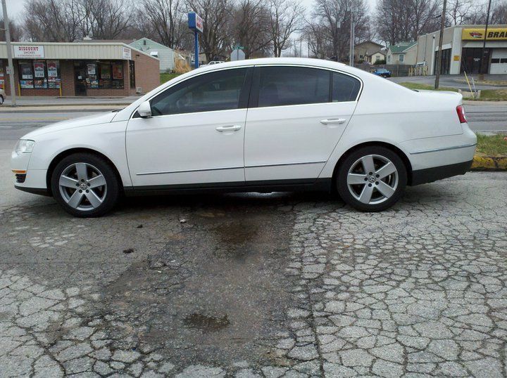 White sedan parked on a cracked lot in front of storefronts
