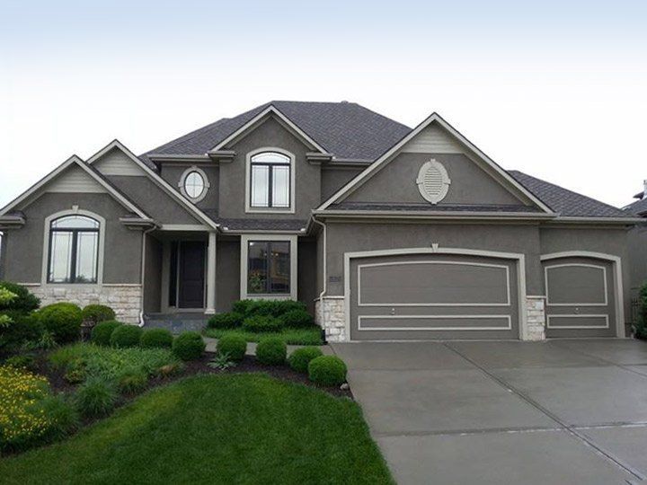Suburban two-story gray house with a wide driveway, manicured lawn, and attached garage.