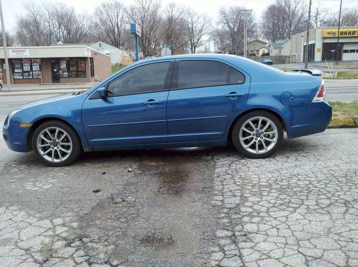 Blue sedan parked on a cracked street near storefronts on an overcast day