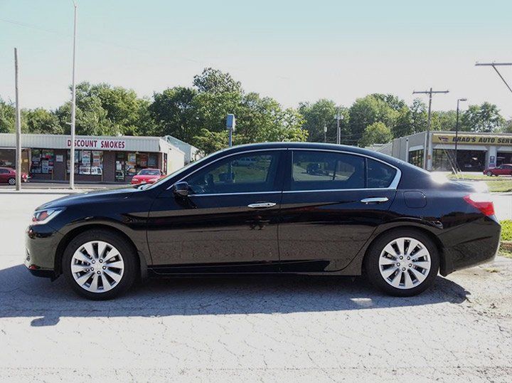 Black sedan parked in a lot with trees and buildings in the background