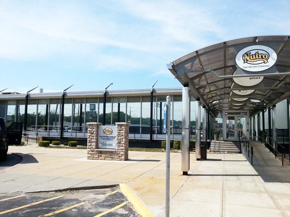 Modern commercial building entrance with glass facade, covered walkway, and parking lot sign