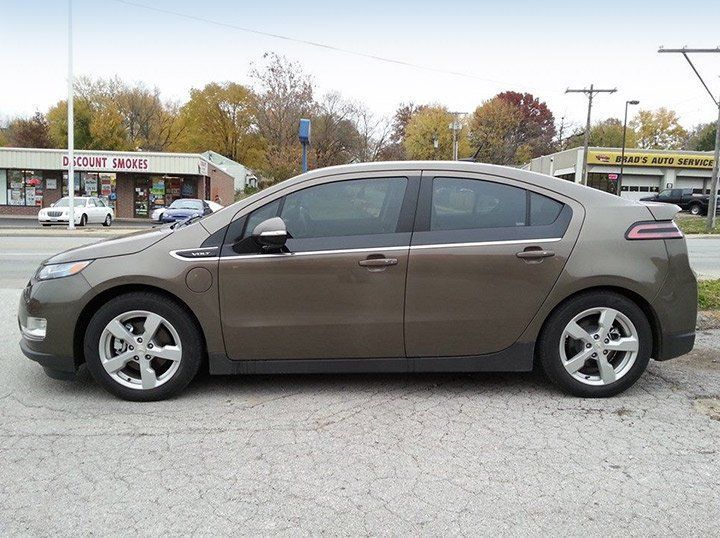 Side view of a brown sedan parked in a lot with buildings and trees in the background.