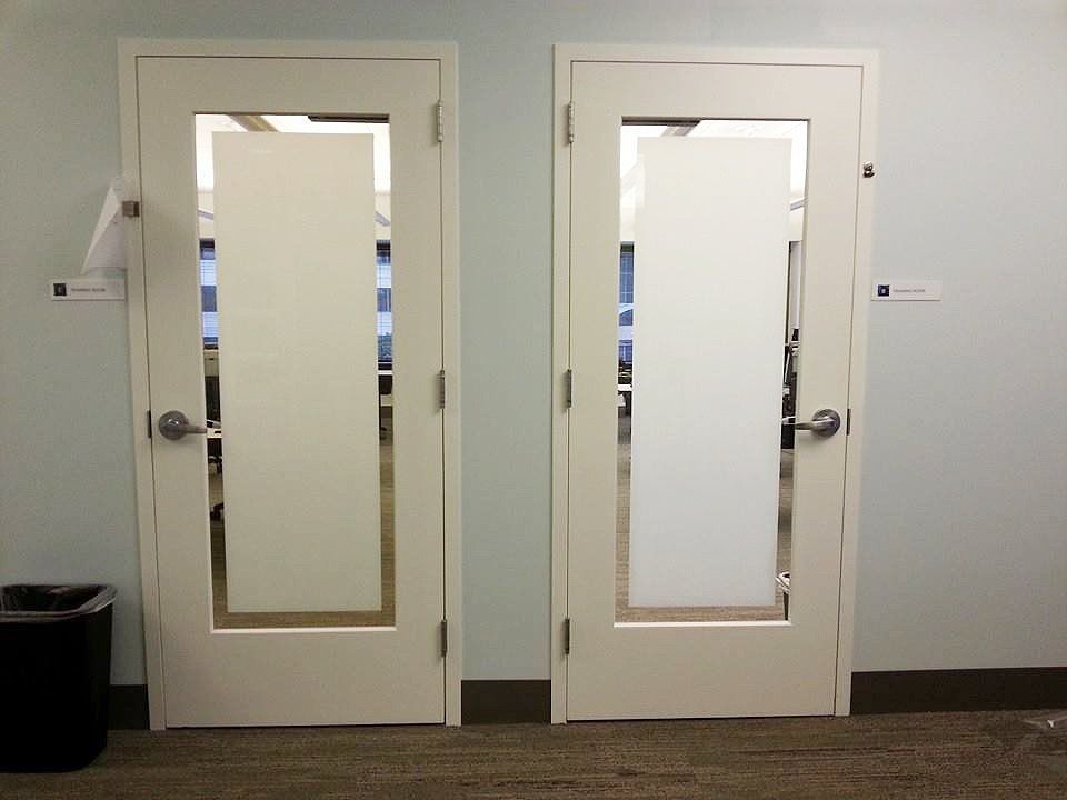 Two white office doors with narrow glass windows in a hallway
