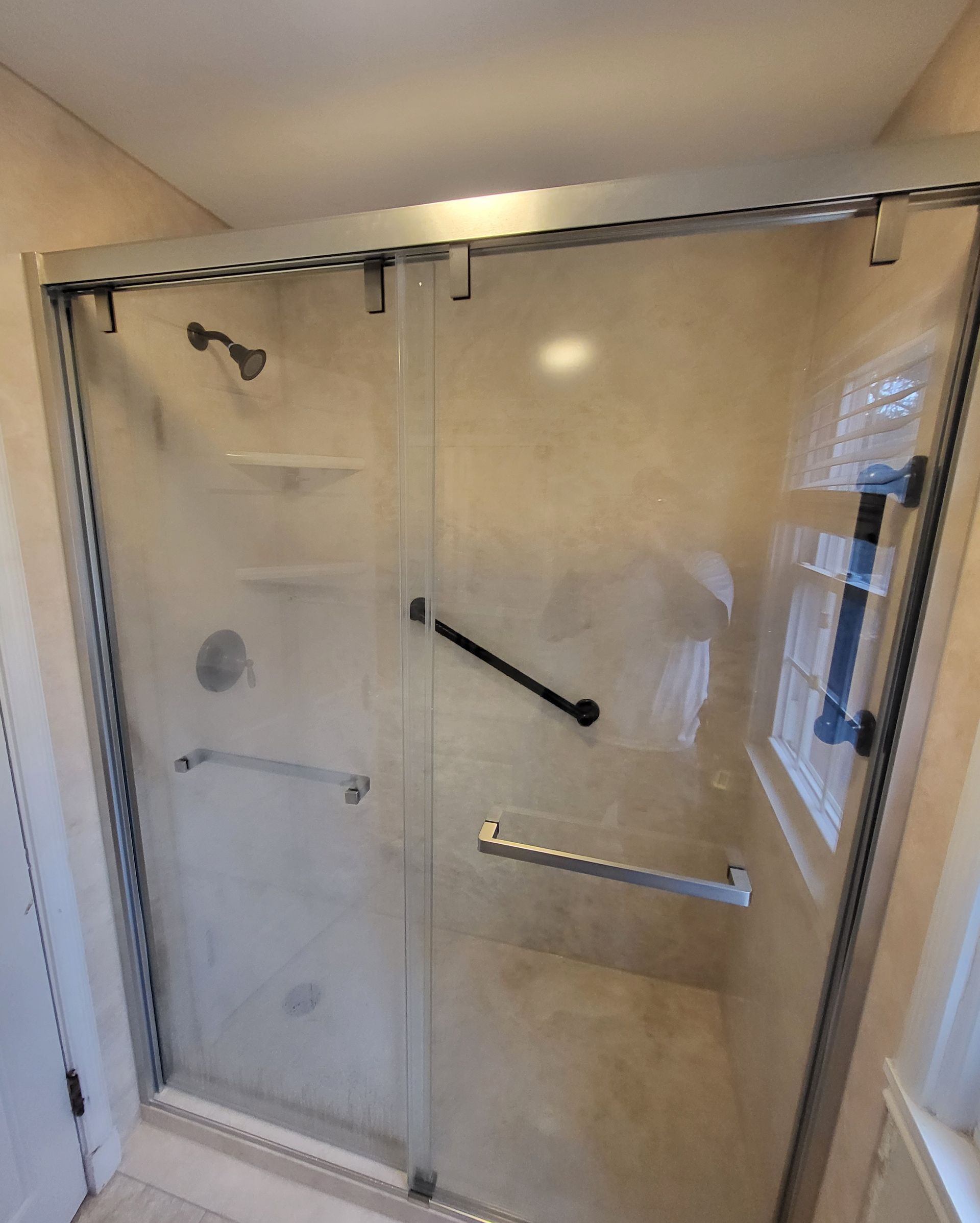 Glass shower stall with grab bars in a bathroom.