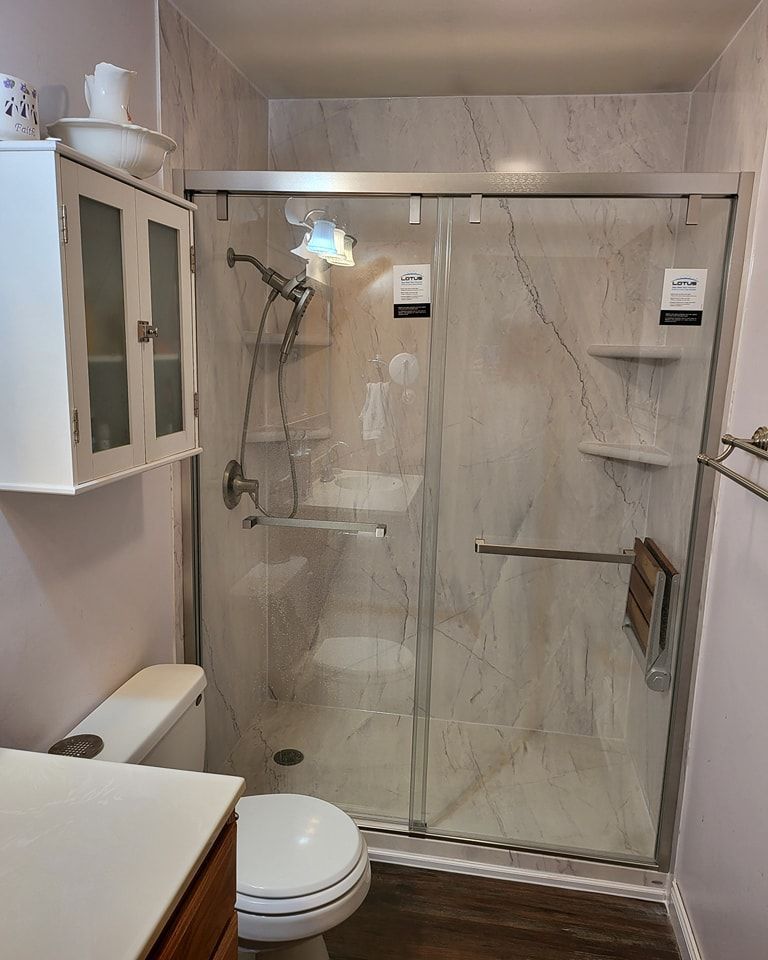 Bathroom with a glass shower, toilet, and cabinet. Light-colored walls, a dark floor, and a white toilet.