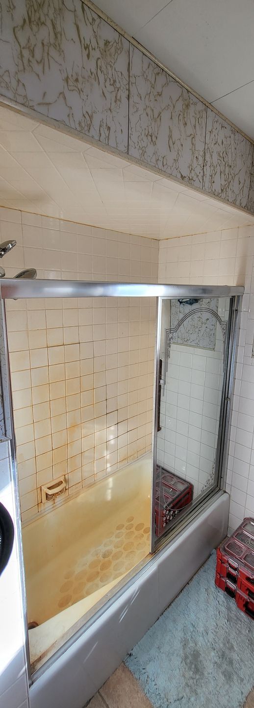 A dilapidated, dirty shower stall with stained tiles and a metal frame.