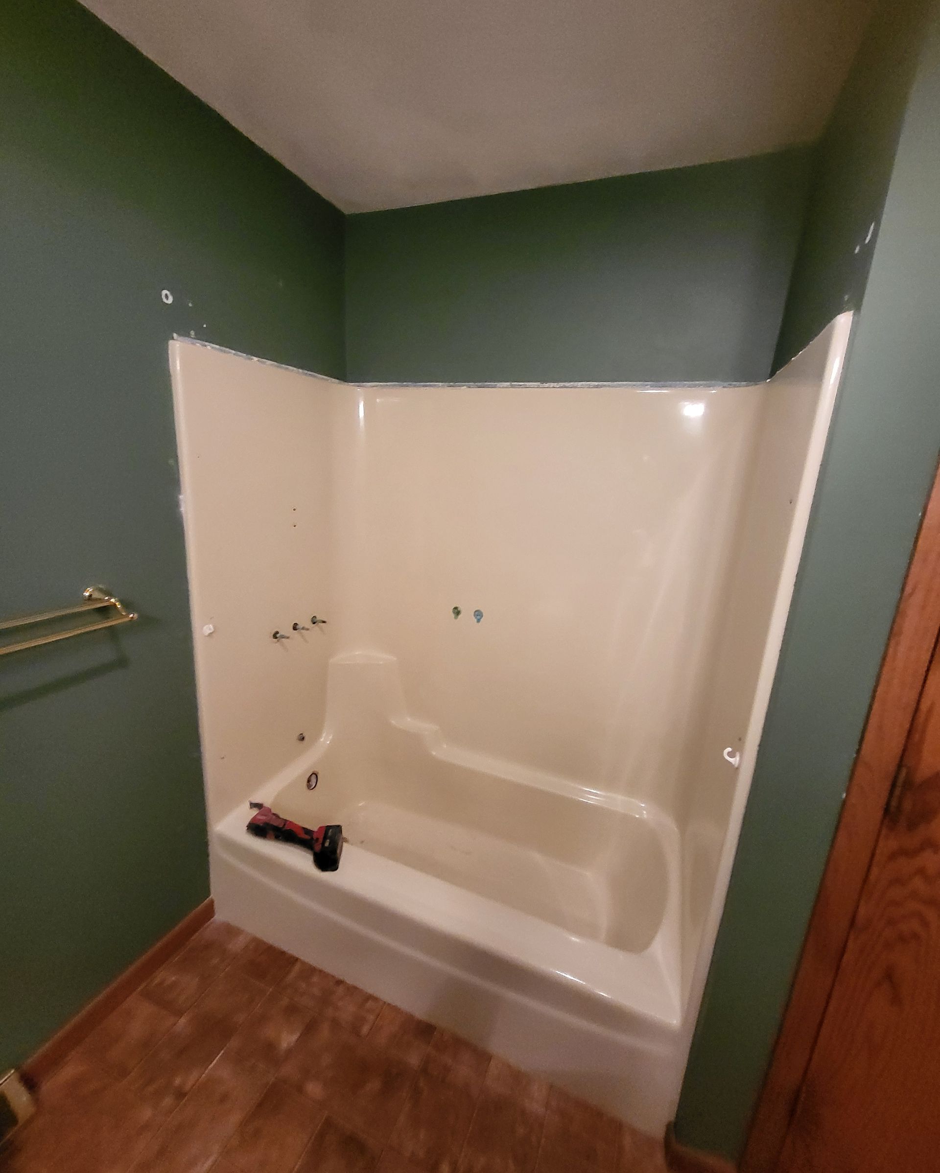 A beige bathtub against green walls in a bathroom with brown flooring and a brown door.