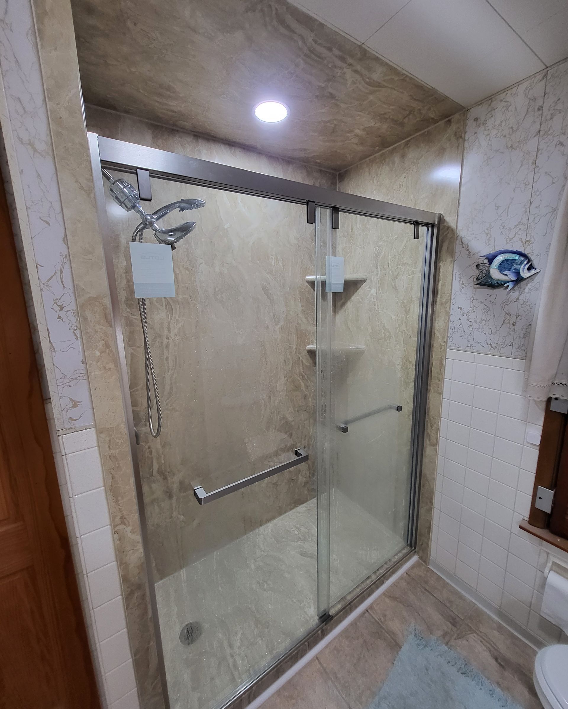 Shower stall with glass doors, grab bar, and tiled walls.