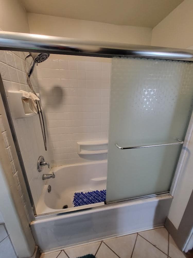 White bathtub with sliding glass doors, shower head, and white tile.