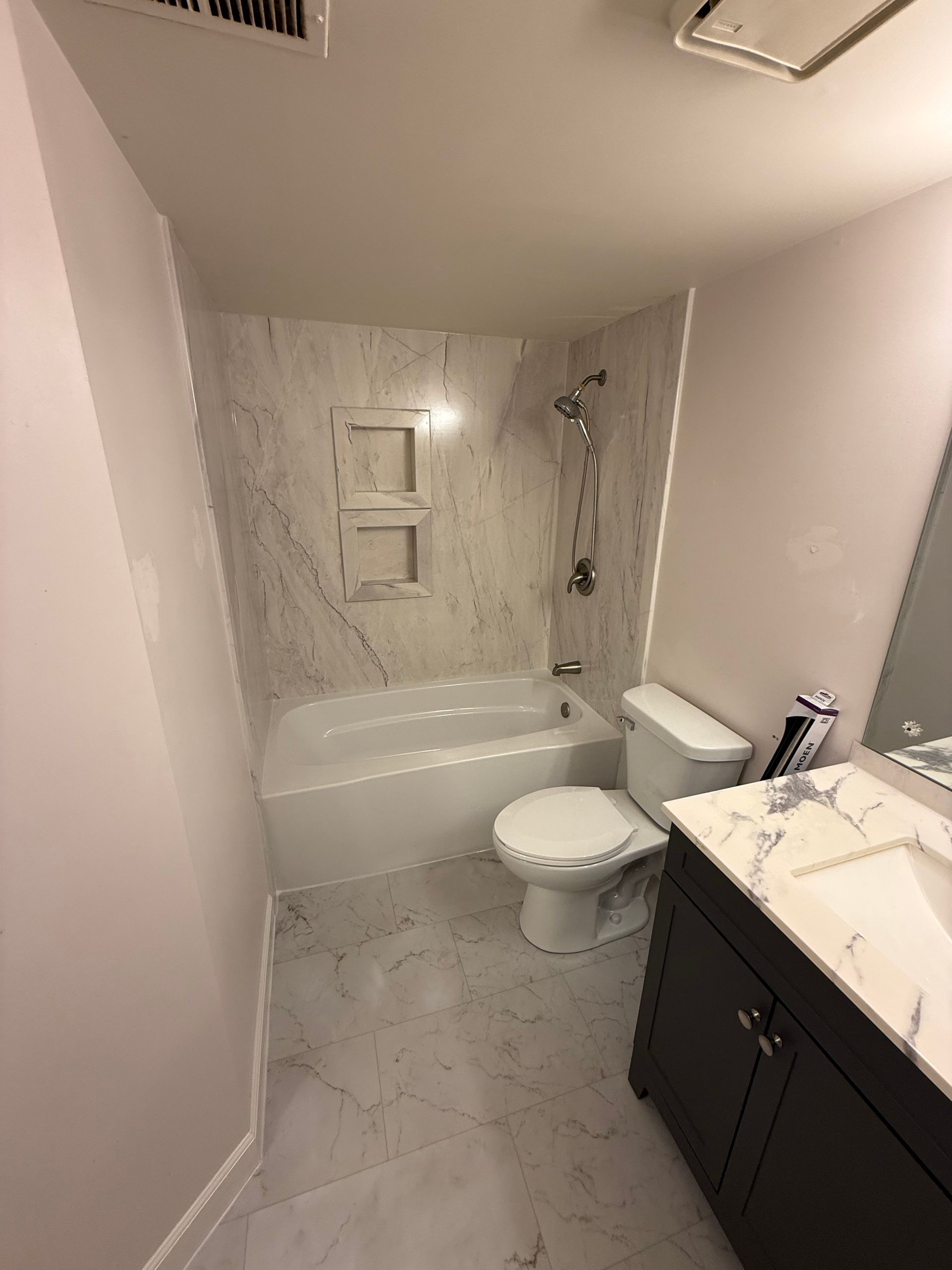 Bathroom with white tub, toilet, and sink; marble-like shower surround, and dark brown vanity.