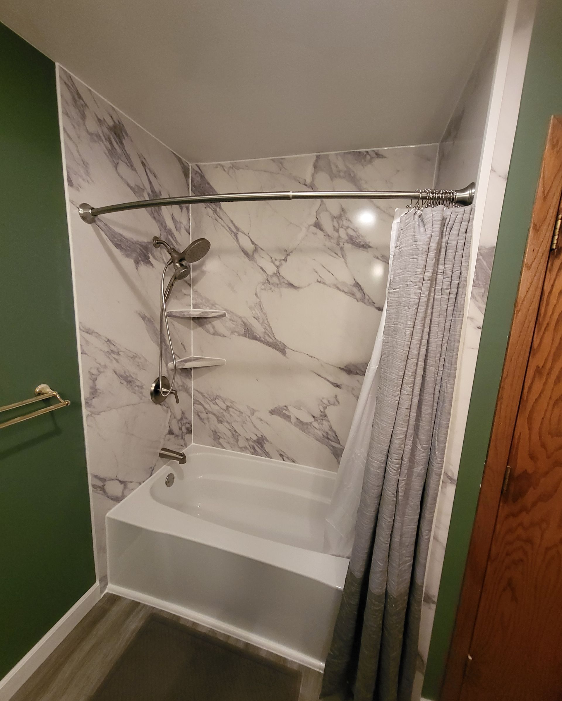 Bathroom with white tub, marble-look shower wall, shower curtain, and green wall.