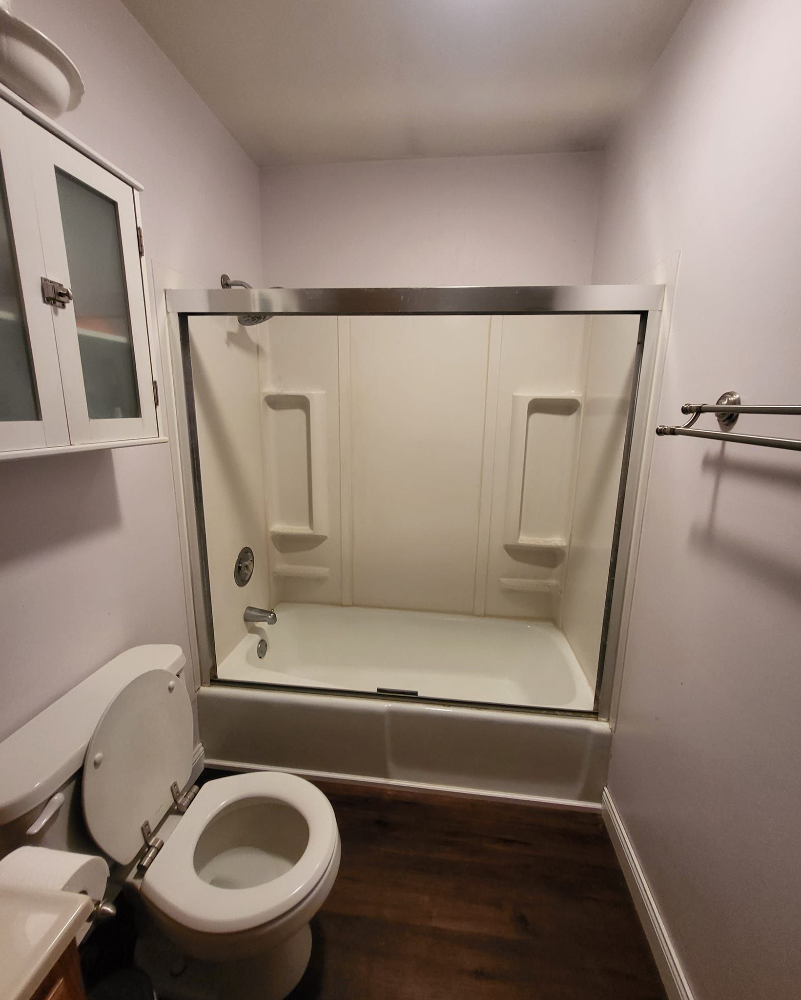 A small bathroom with a toilet, shower, and cabinet. Purple walls, dark floor, and white fixtures.