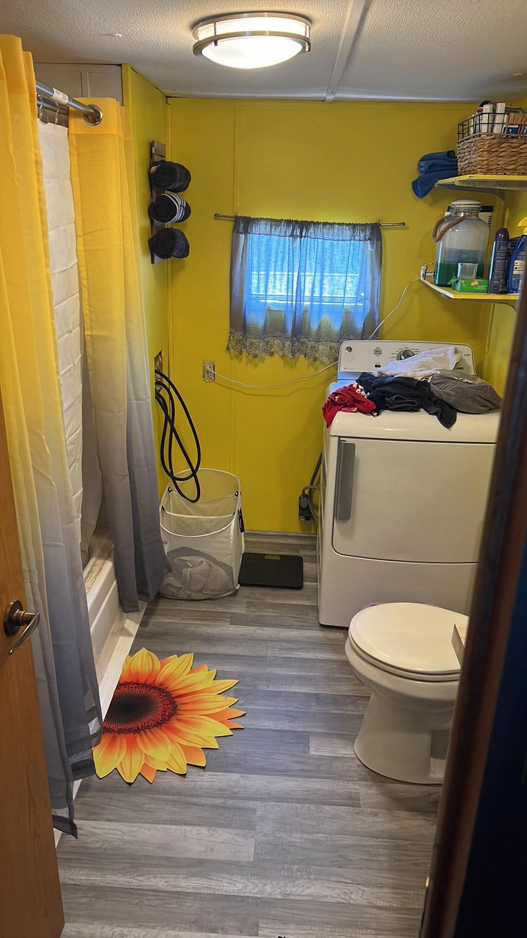 Small bathroom with yellow walls, a sunflower rug, and a washing machine; shower curtain visible.
