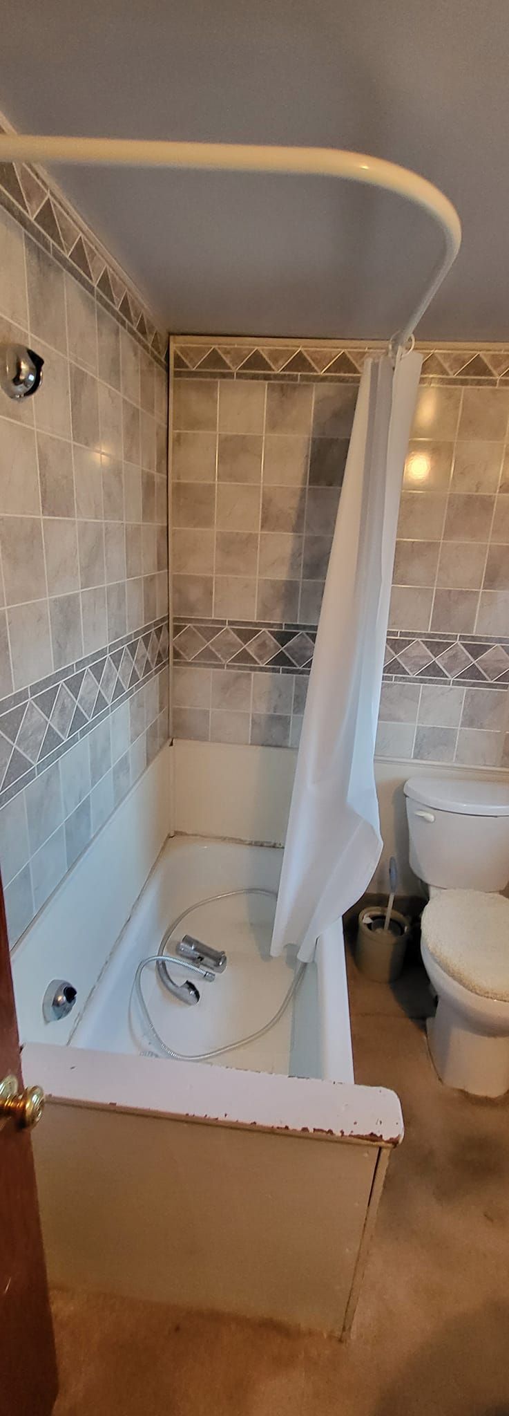 A bathroom with a bathtub, toilet, and shower curtain. Tile walls and brown flooring are visible.