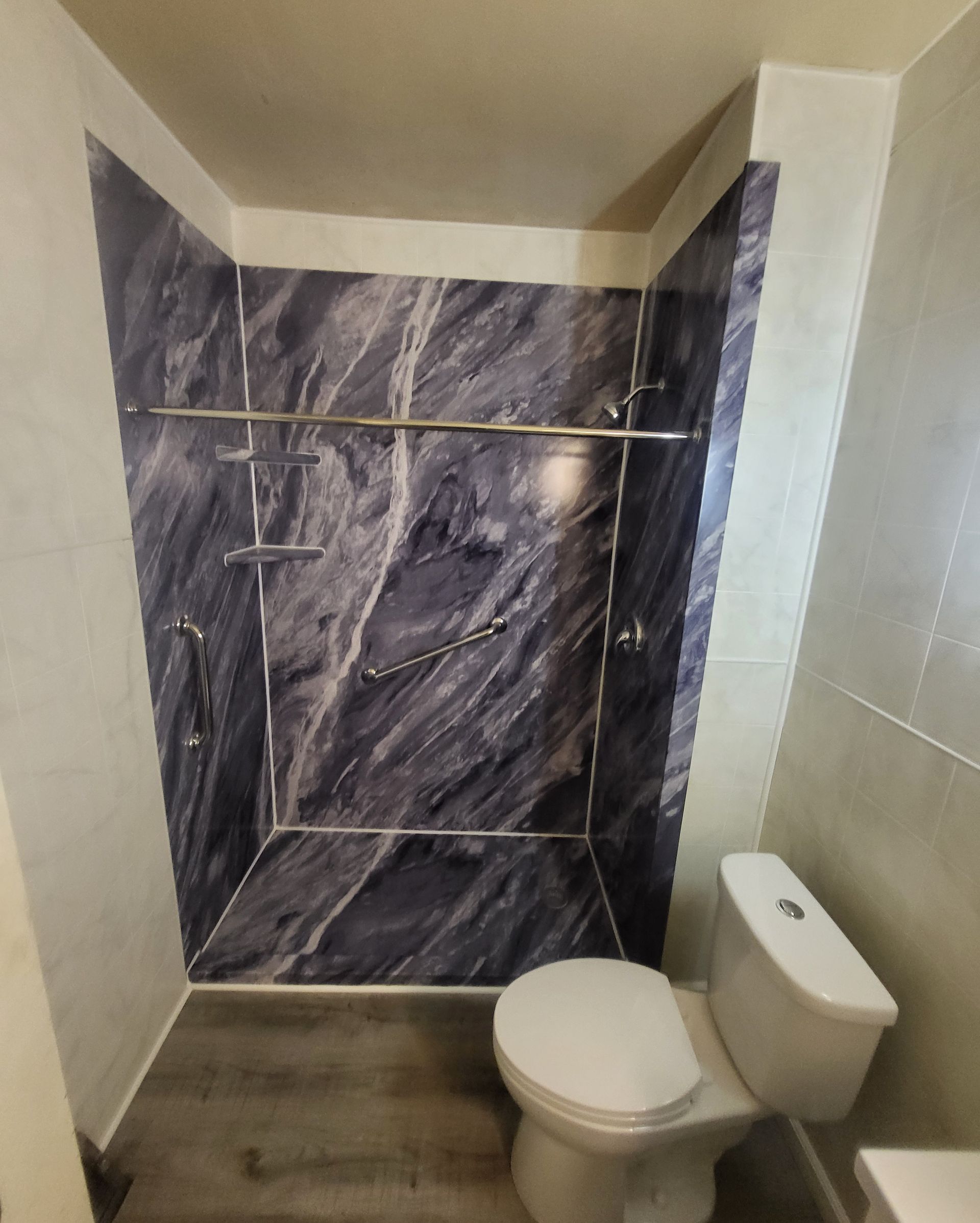 A small, modern bathroom with a marble-patterned shower, toilet, and neutral-colored walls.