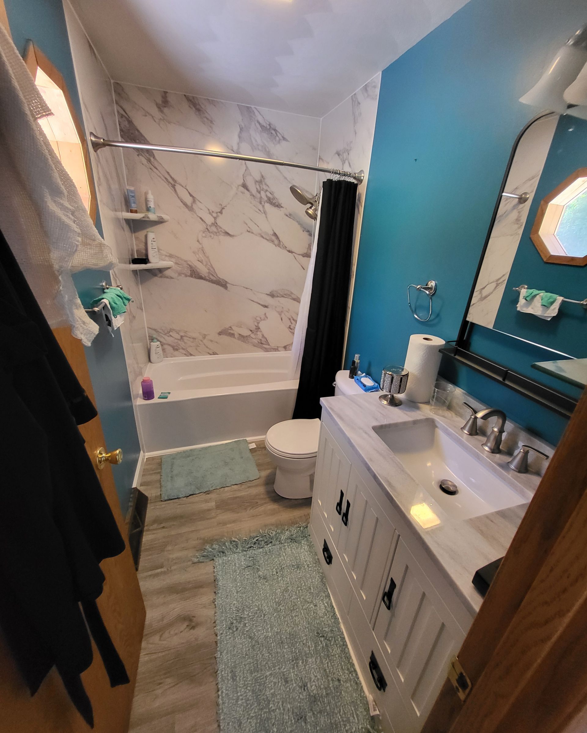 Bathroom with marble shower, teal walls, white vanity, and blue rug.