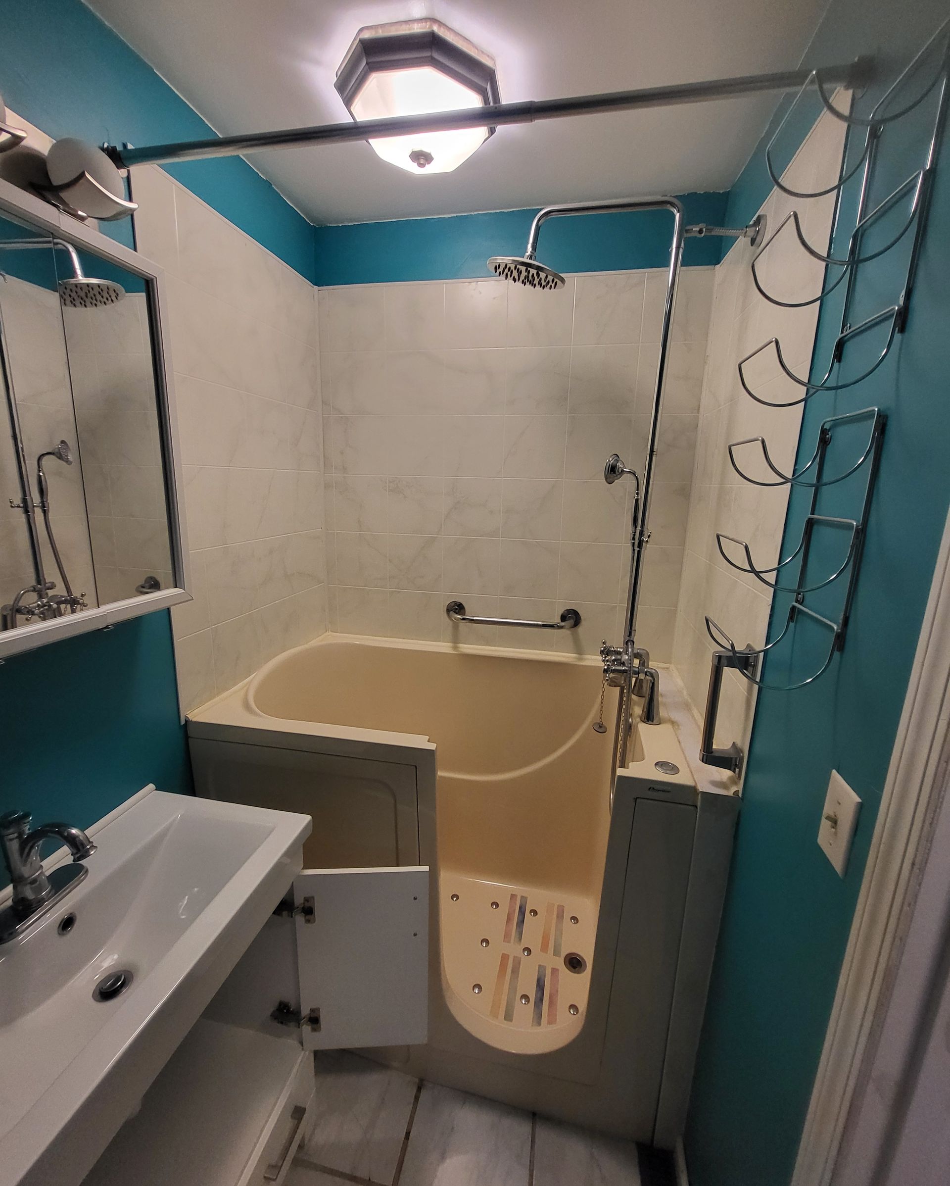 Small bathroom with a walk-in tub, sink, and showerhead. Teal walls, white tiles, and chrome fixtures.