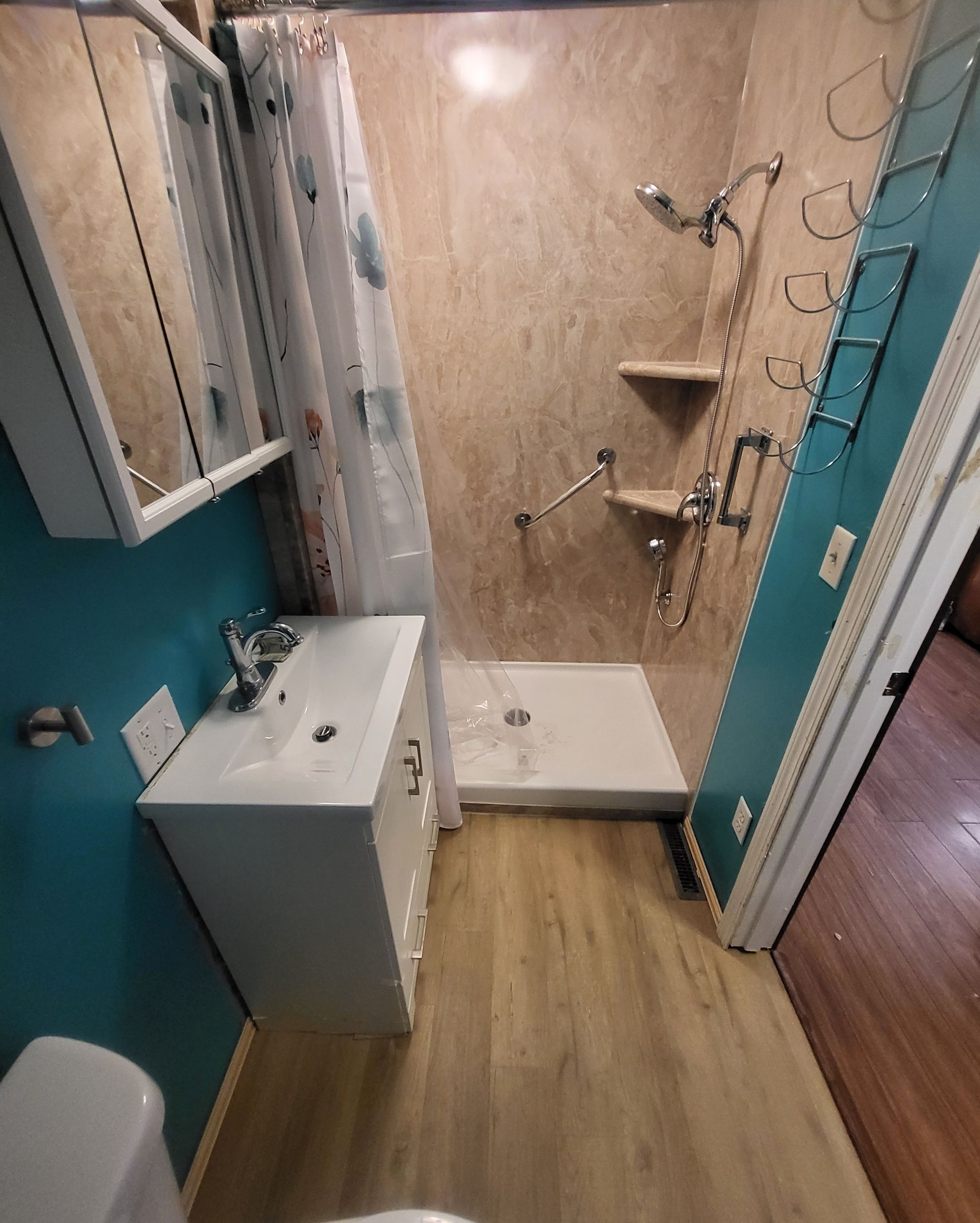 Small bathroom with teal walls, beige shower, white vanity, and light wood floor.