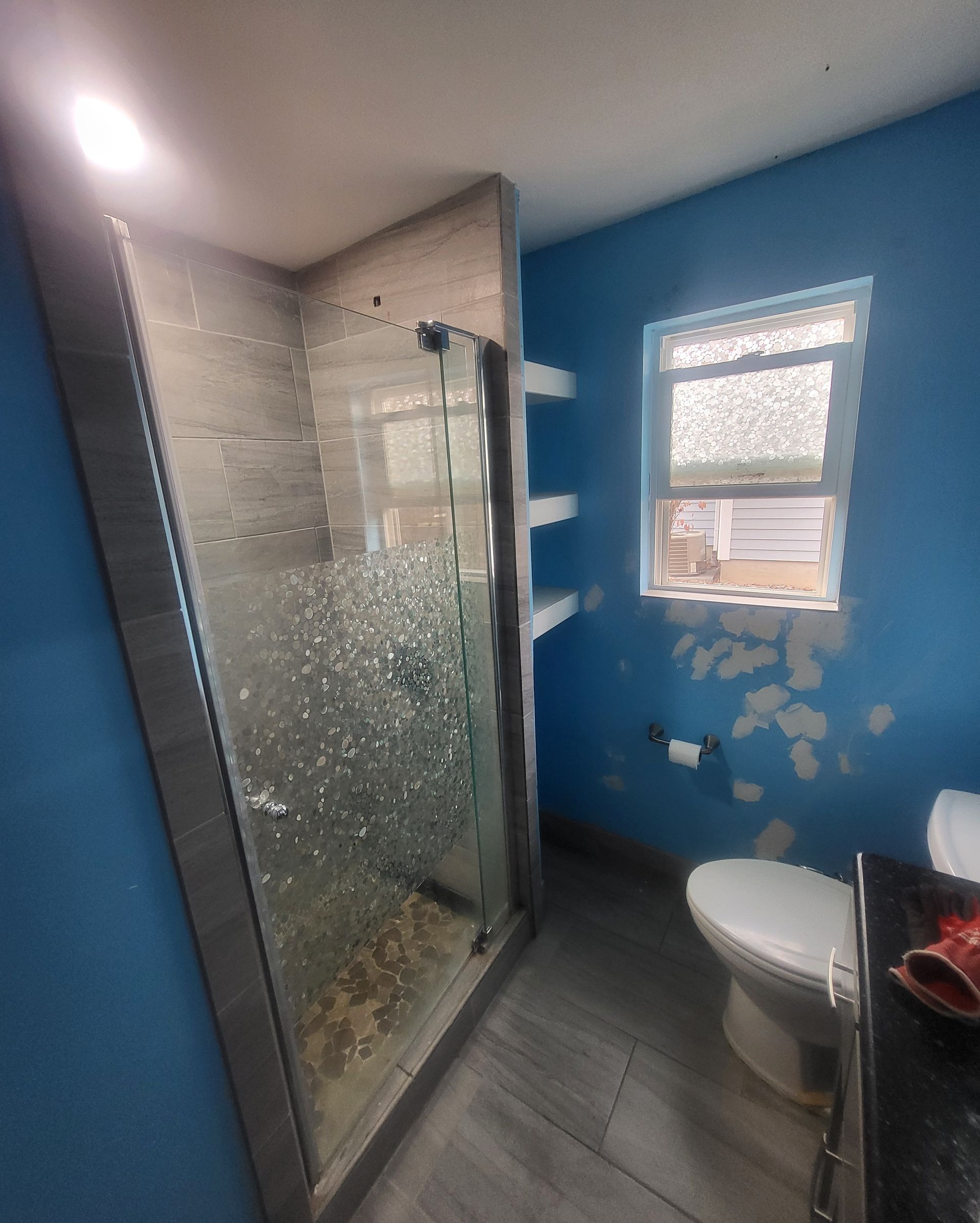 Bathroom with blue walls, glass shower, and toilet. Paint is peeling near the window.
