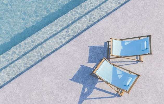 Poolside scene with two light blue lounge chairs casting shadows, next to a pool.