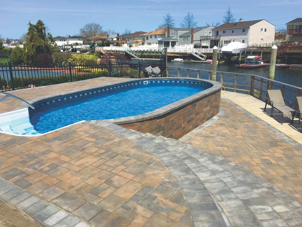 Pool with blue water and brick border, set in a backyard with a canal view and patio stones.