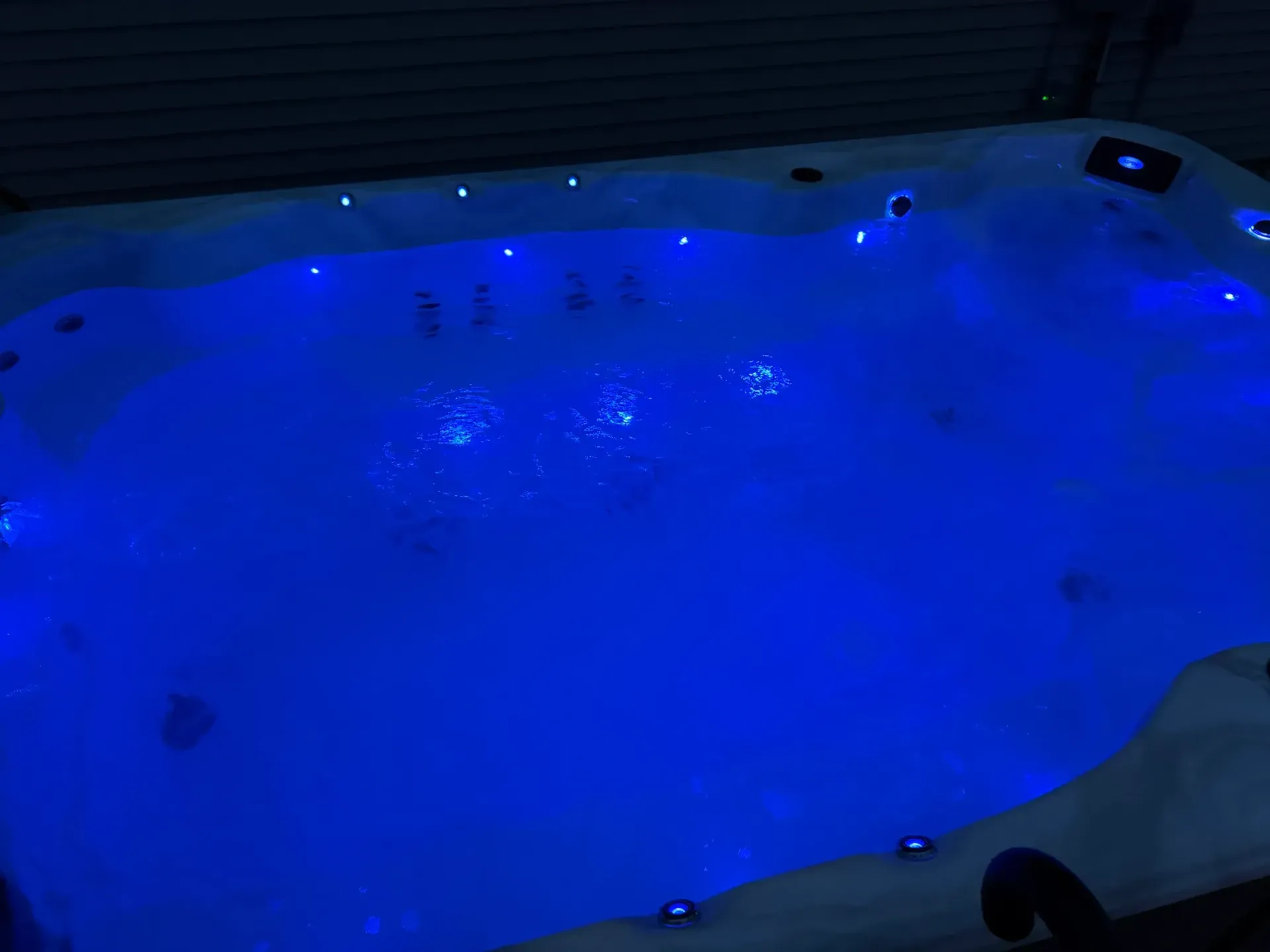Lit-up hot tub with blue lights, bubbling water, and dark surrounding area.