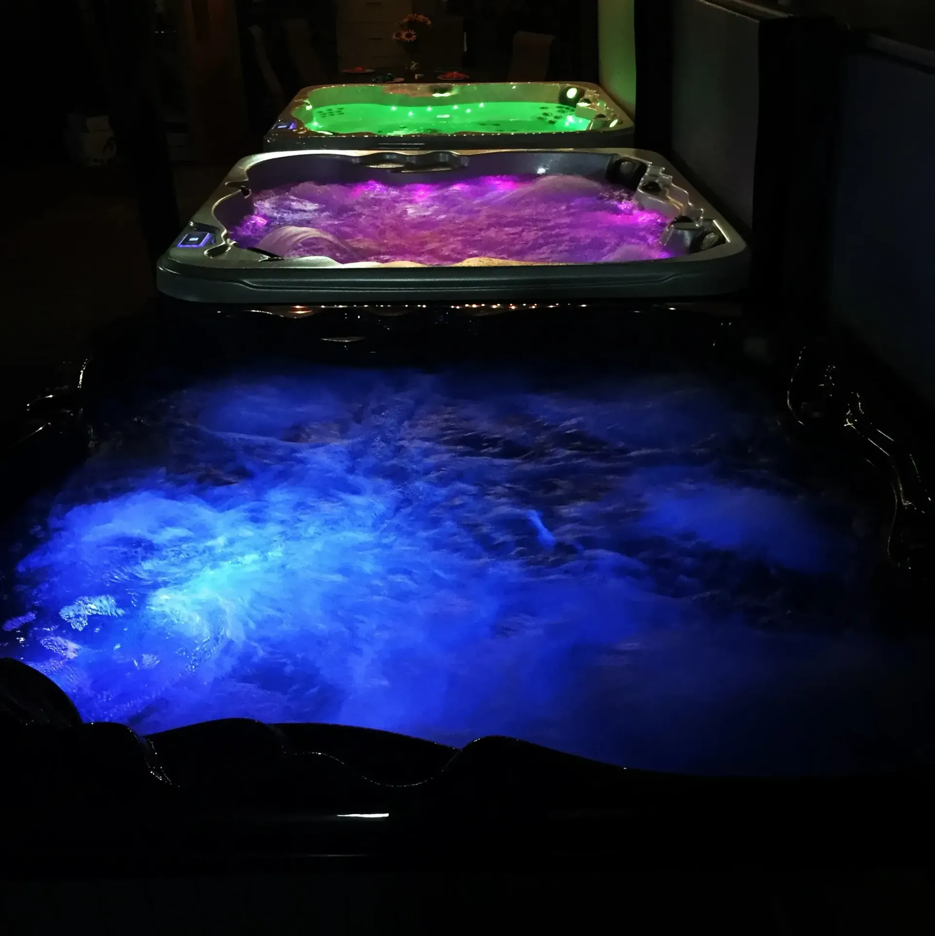 Three hot tubs lit with blue, purple, and green lights at night.